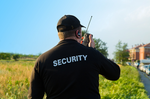 A security guard walks the perimeter of an outdoor event while using his radio.